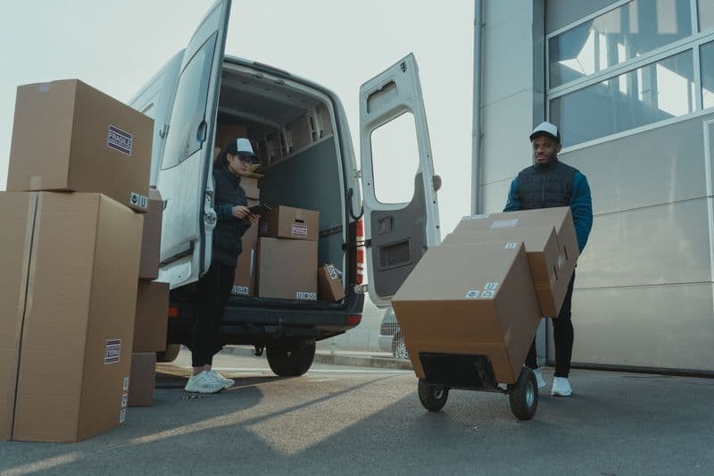 Two logistics workers loading parcels into a delivery van at a depot